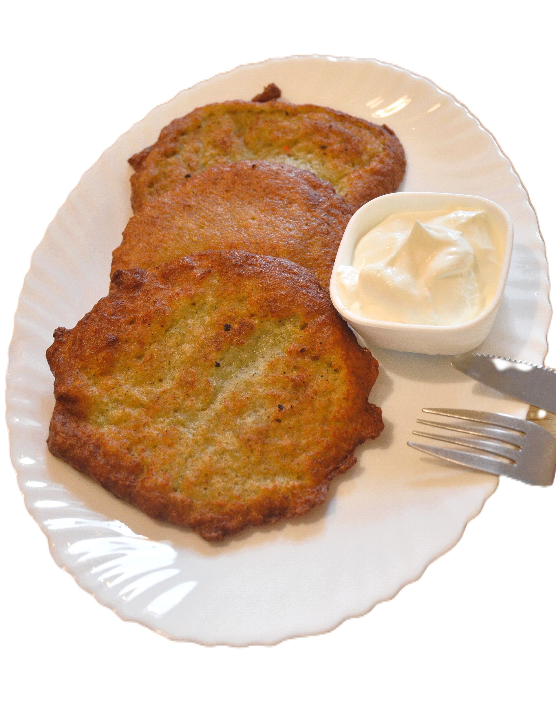 Tortitas de papa en un plato, al lado un tazoncito con crema espesa