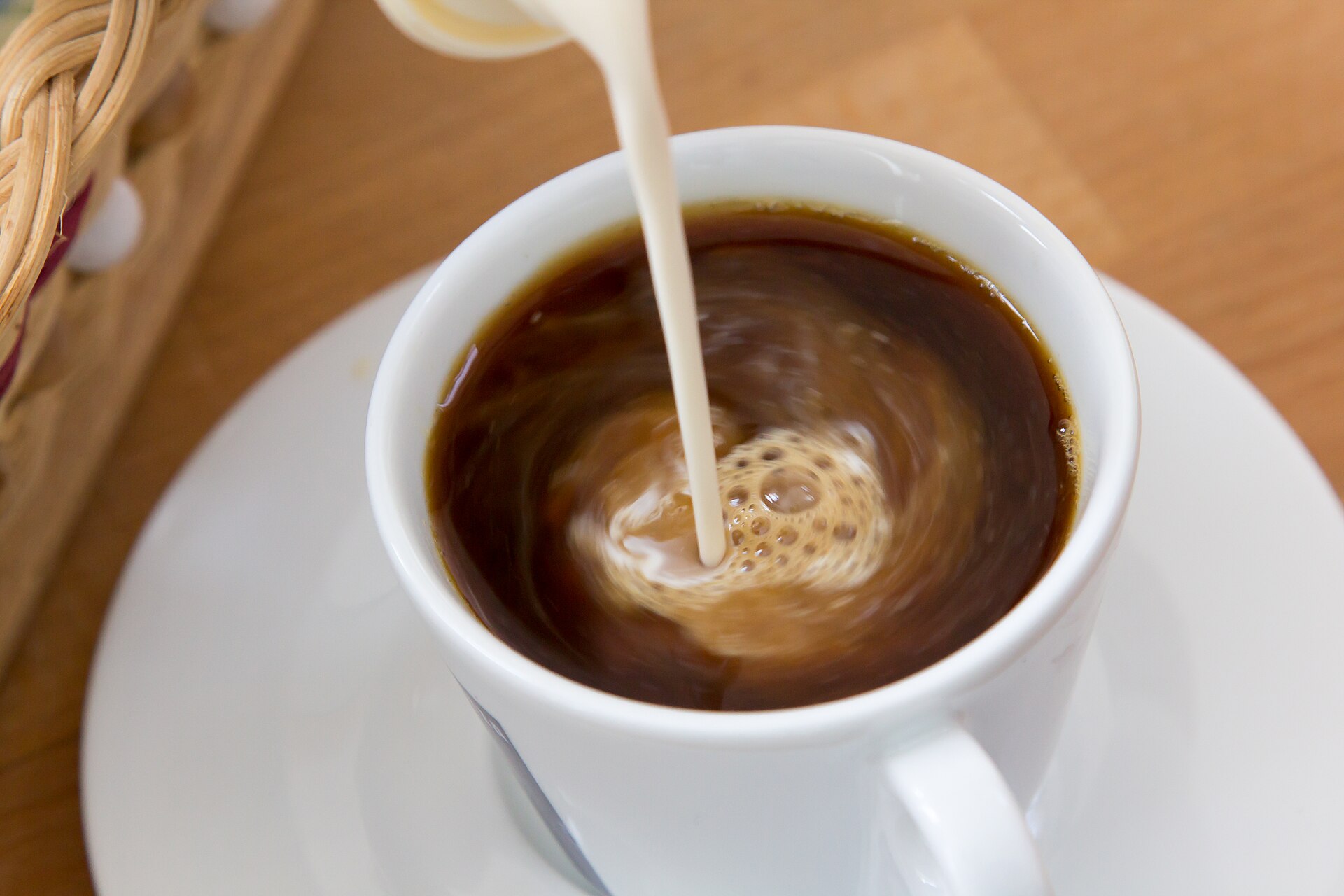 Leche evaporada cayendo en una taza blanca de café negro