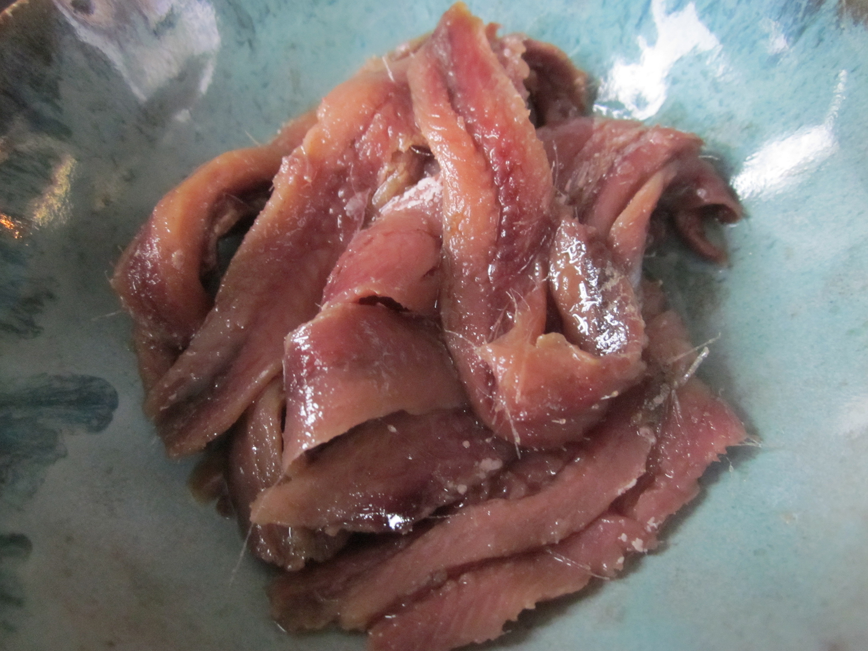 Un puño de filetes de anchoa en aceite dentro de un tazón