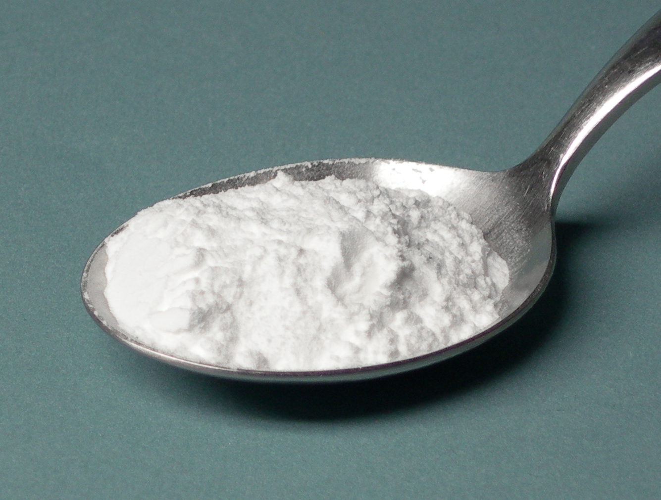 Una cucharadita colmada de polvo para hornear blanco sobre fondo verde