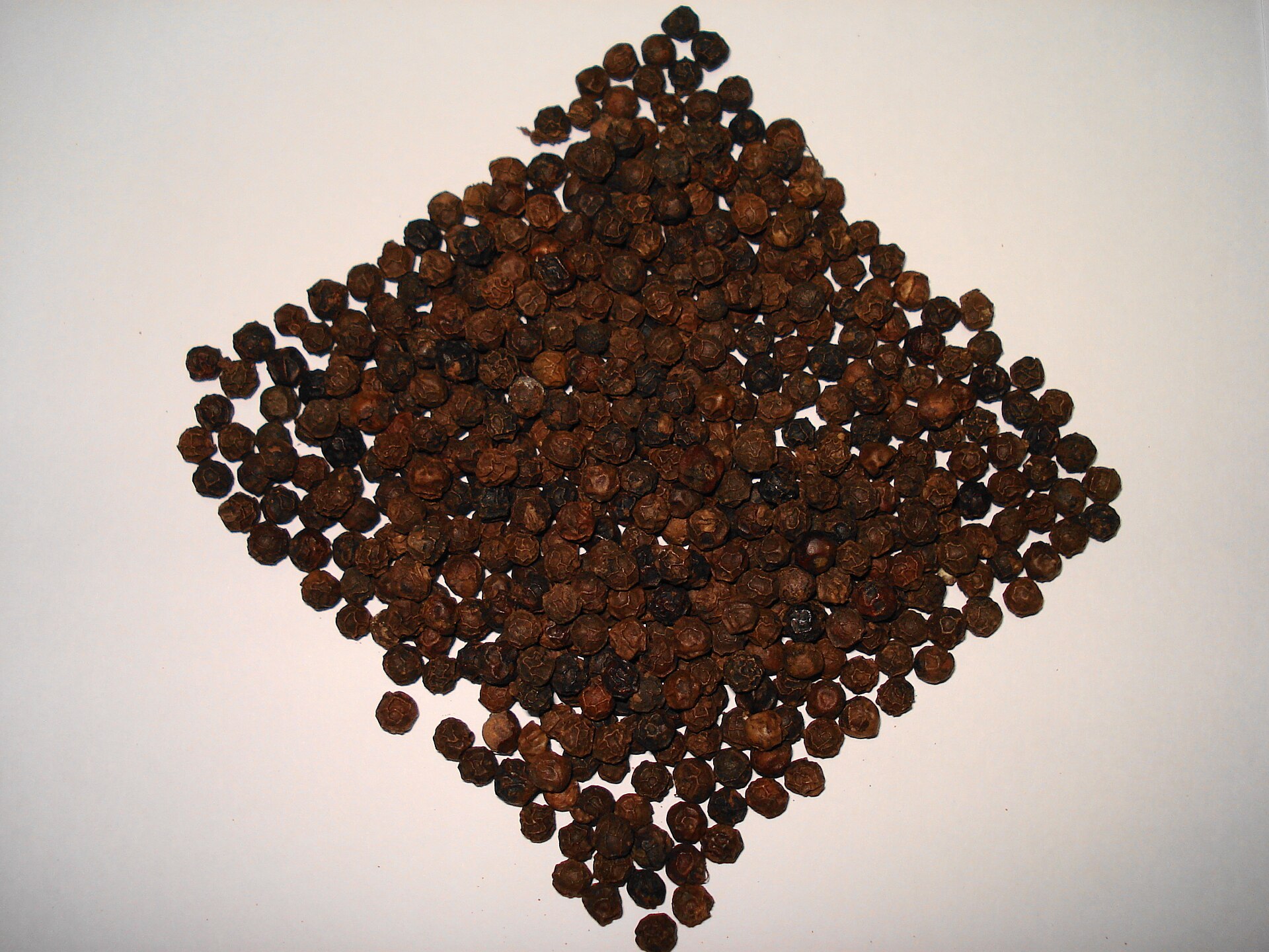Granos enteros de pimienta negra de cerca, arrugados y café oscuro