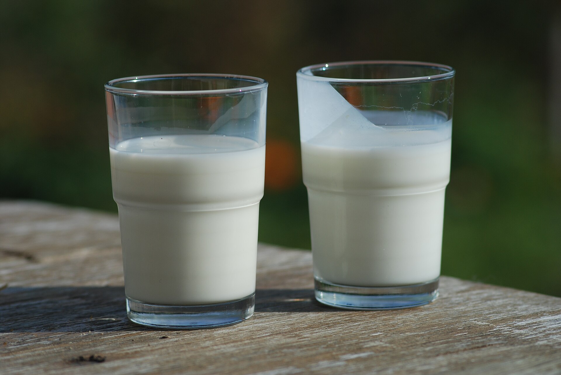 Dos vasos lado a lado sobre una tabla de madera, suero de mantequilla a la derecha y leche a la izquierda