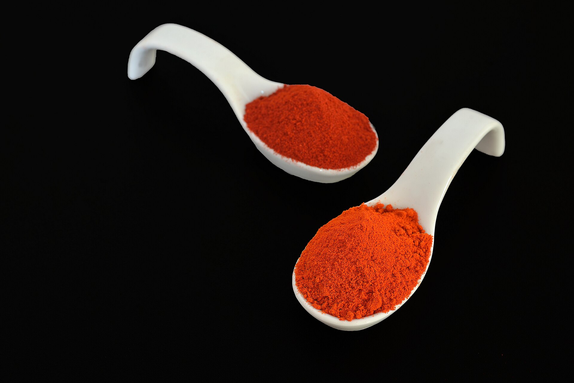 Dos cucharas blancas con pimentón rojo molido sobre fondo negro