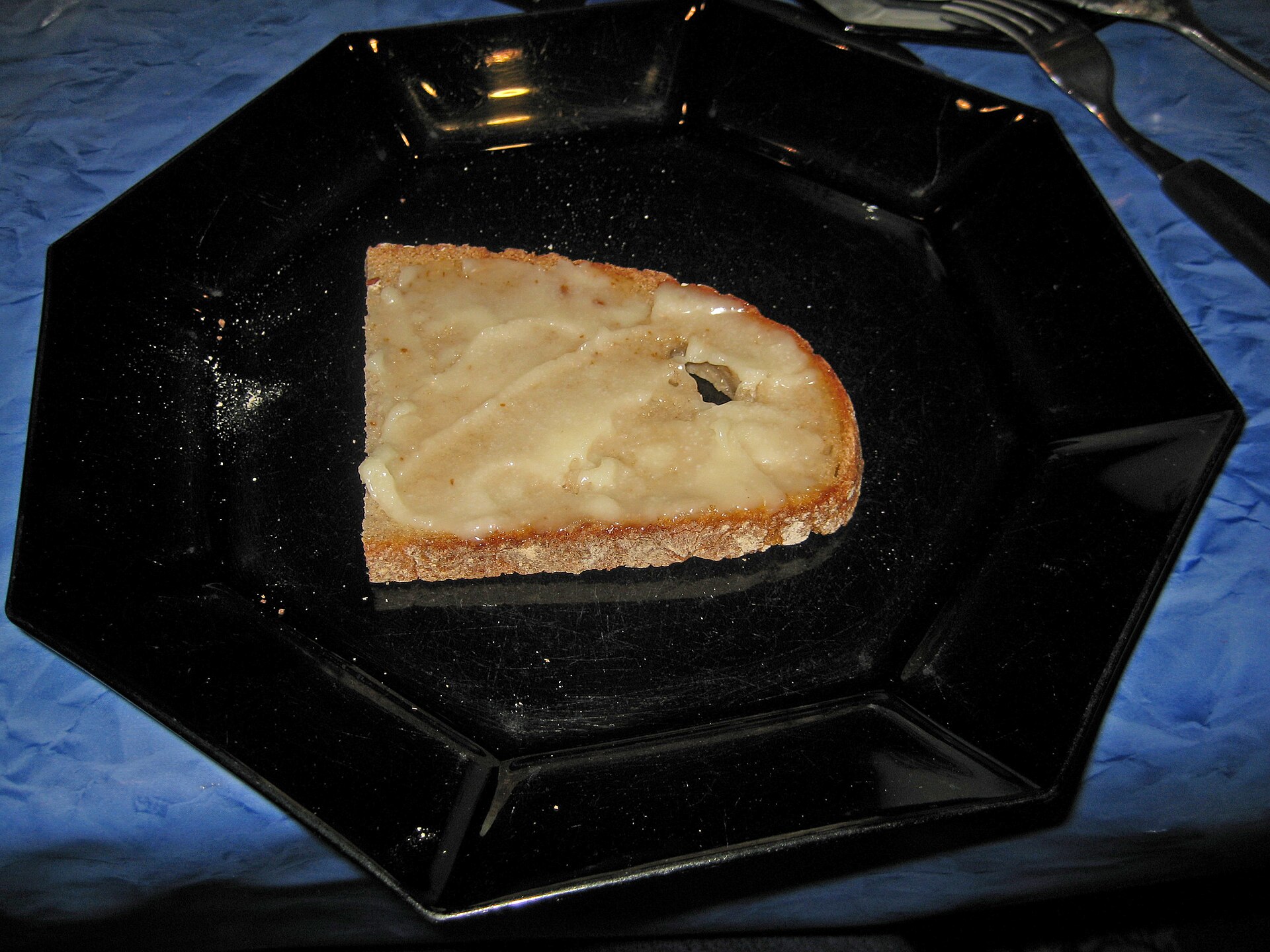 Una rebanada de pan untada con manteca de ganso clara, en un plato negro