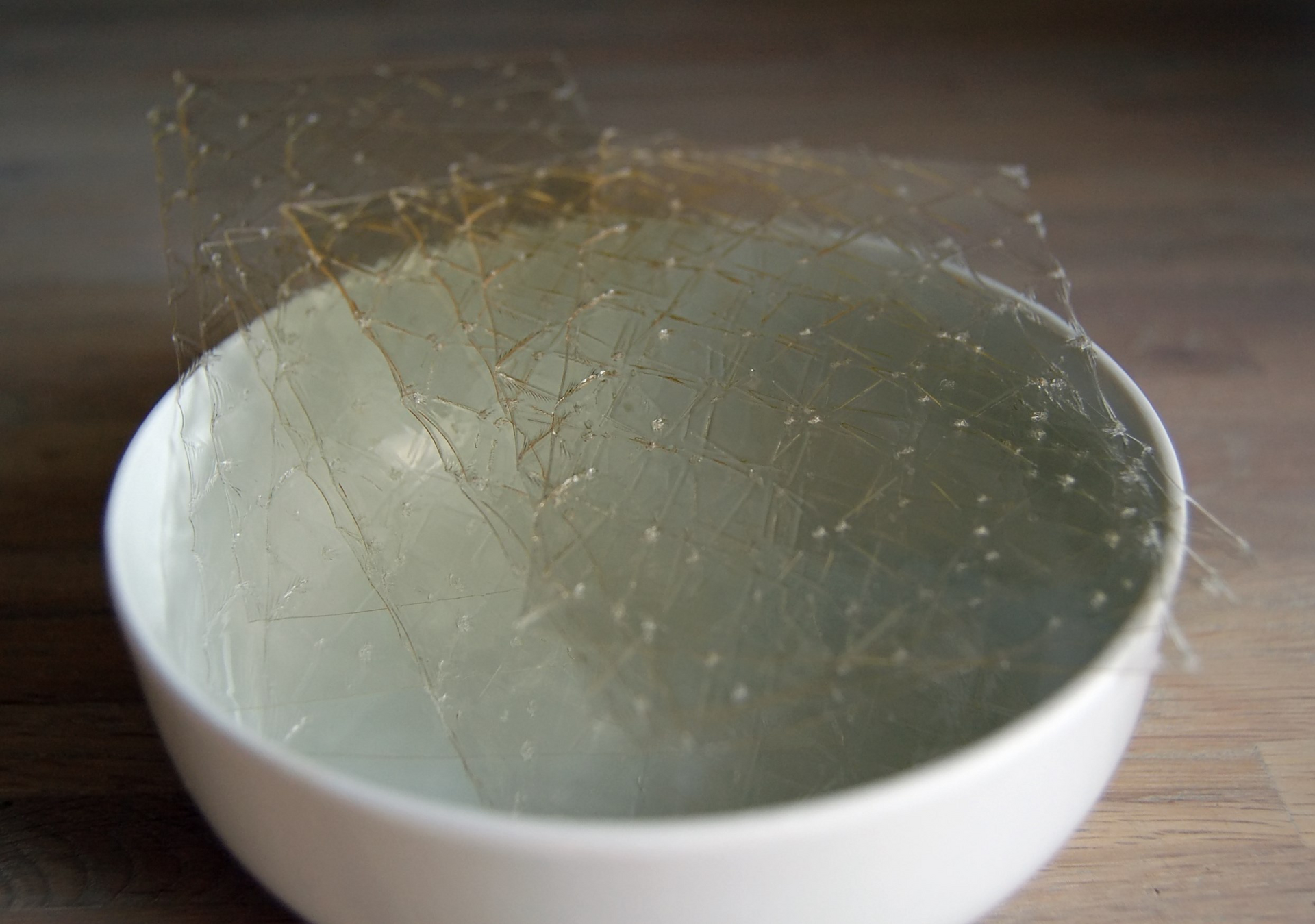 Hojas transparentes de grenetina remojándose en un tazón blanco con agua fría
