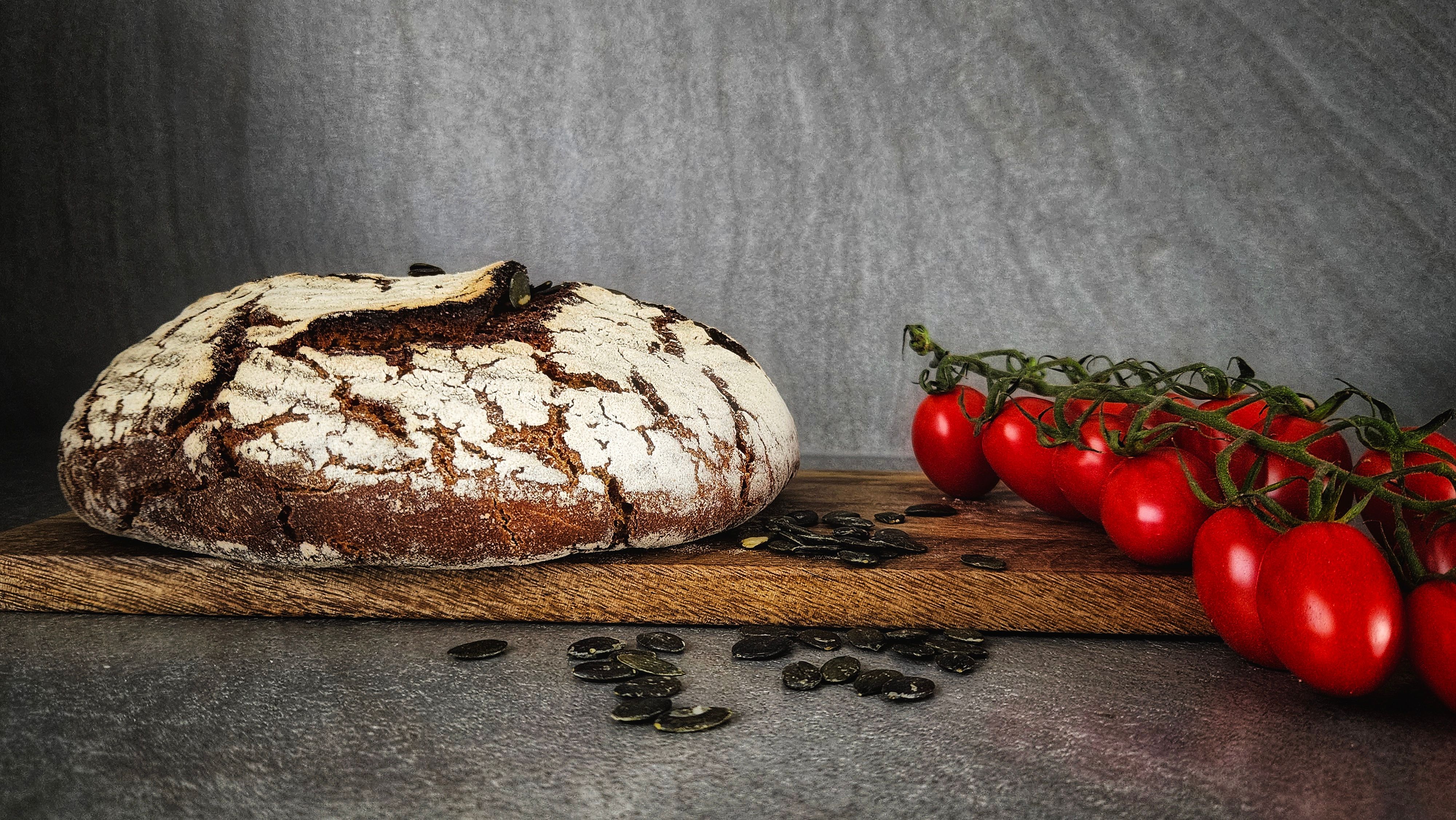 Hogaza de Roggenbrot enharinada sobre una tabla de madera, con jitomates y pepitas de calabaza