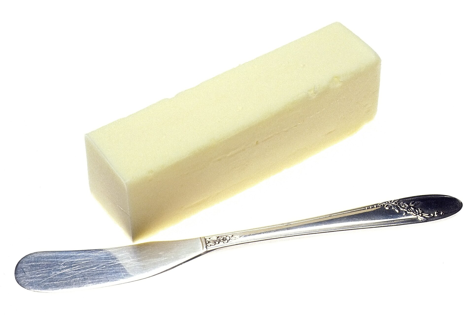 Una barra de mantequilla junto a un cuchillo de untar sobre fondo blanco