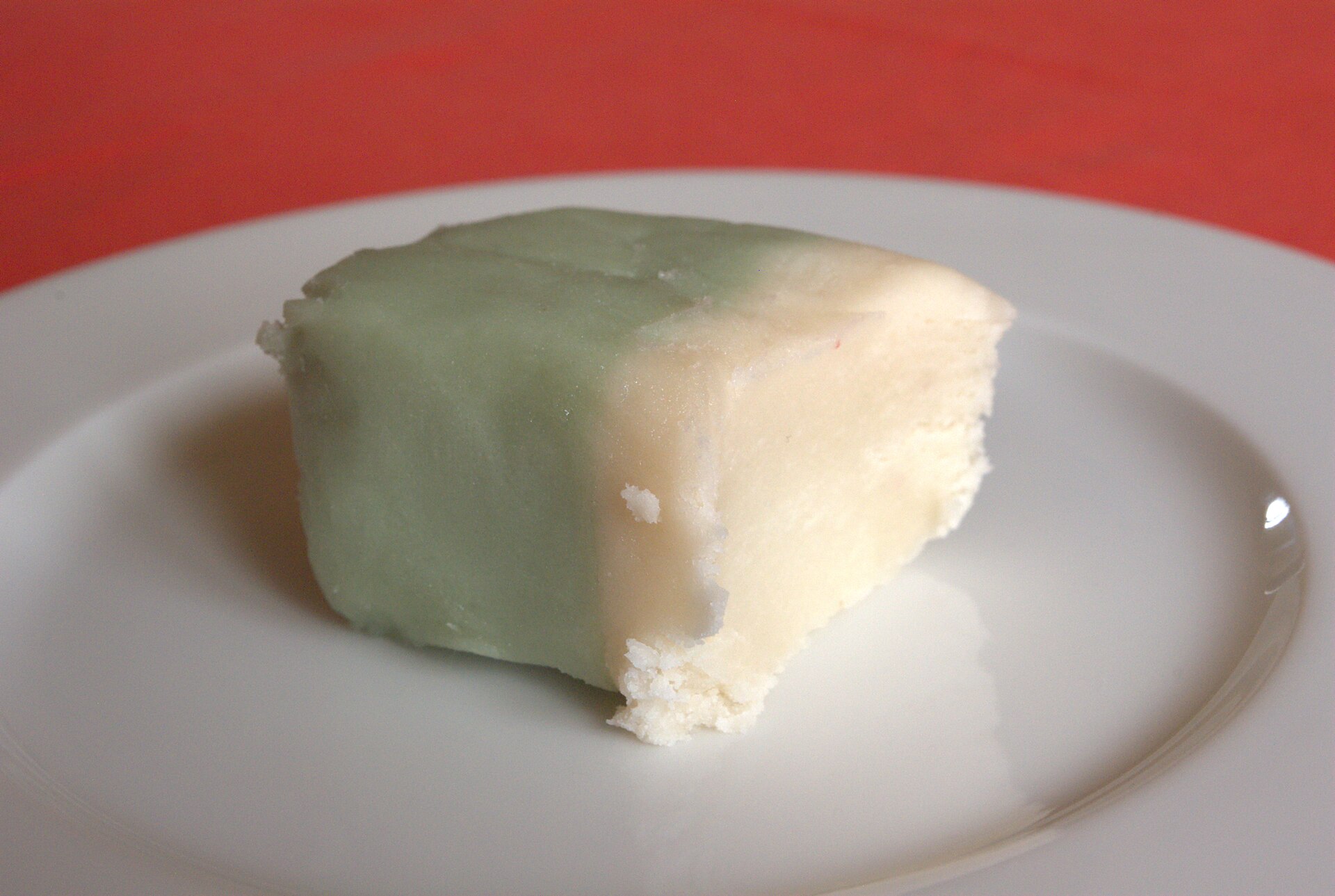 Trozo de mazapán alemán con capa verde; en la orilla rota se ve la masa de almendra clara y húmeda